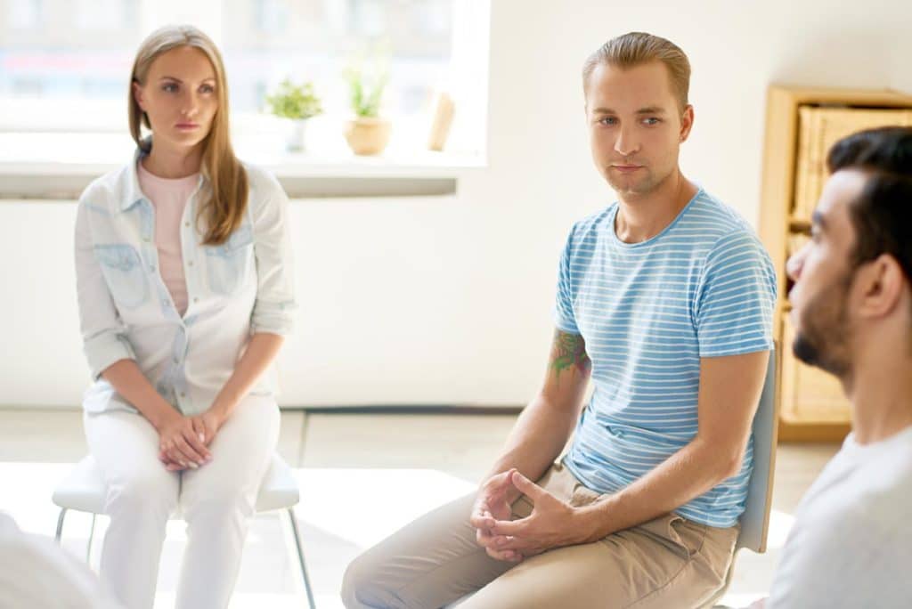 Portrait of modern young man listening intently to other participants of group session sitting in circle sharing trouble discussing non-alcoholic beer