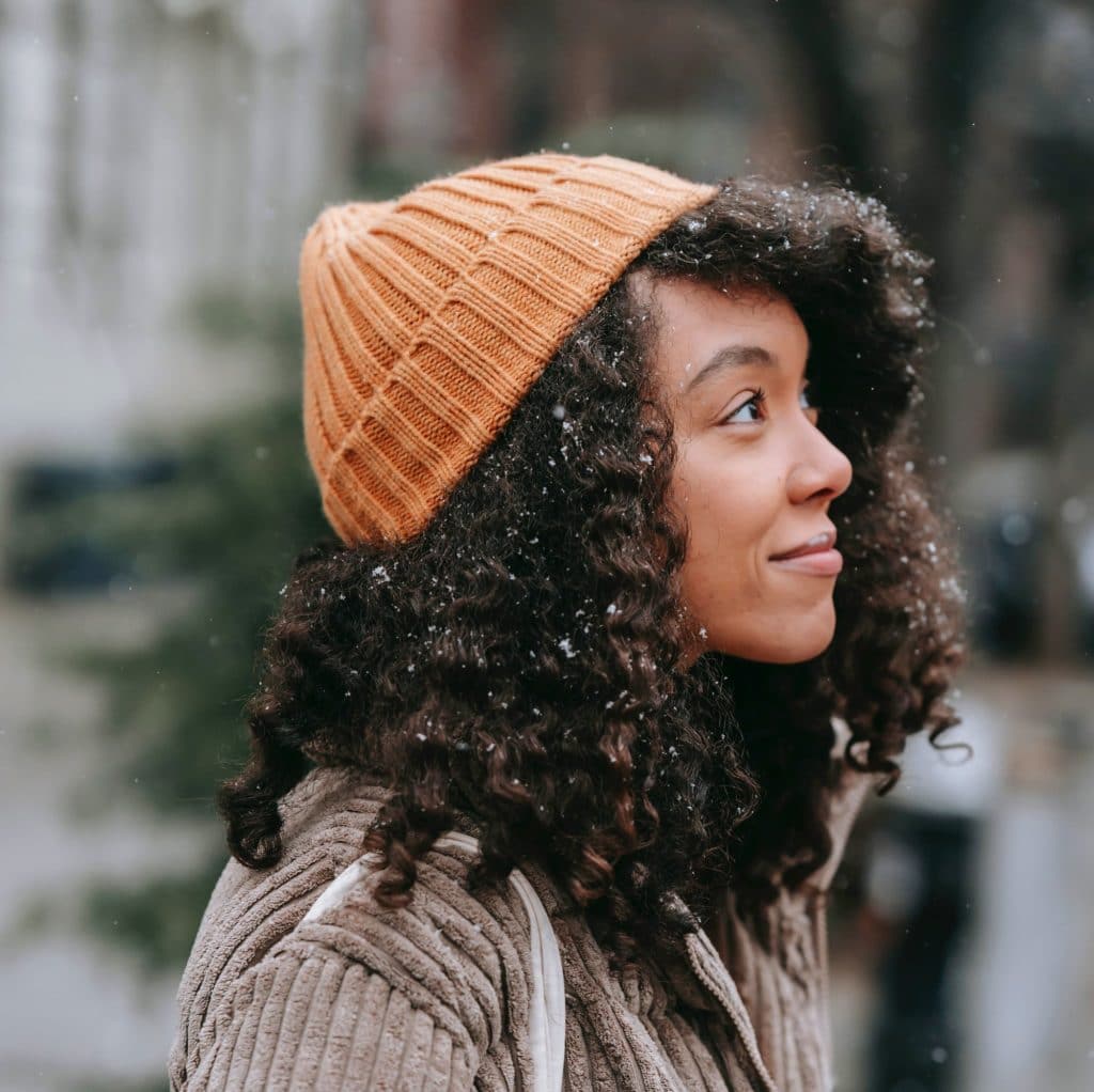 contemplative ethnic woman with curly hair in snowfall
